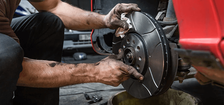 A mechanic fitting a slotted brake rotor to a vehicle with the wheel removed
