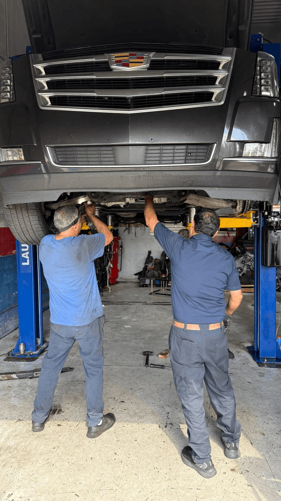 Two technicians at Instant Auto Repair working underneath an SUV raised on a two-post lift