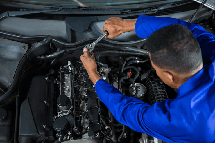 A technician tightening a fitting on an engine with a ratchet, with the hood raised