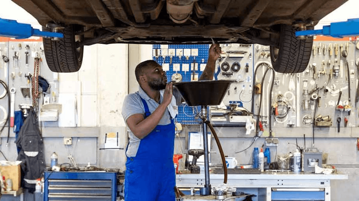 A technician draining engine oil into a collection funnel beneath a vehicle raised on a lift